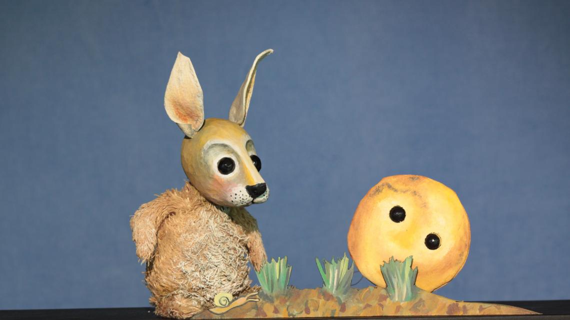 Ein Hase und ein Pfannkuchen mit Augen sitzen im Gras.