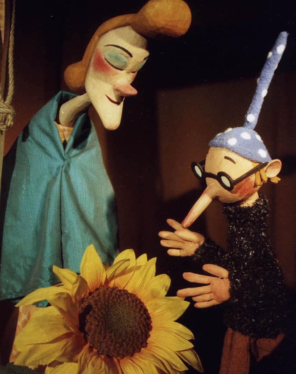 Zwei menschenähnliche Figuren betrachten eine sehr große gelbe Blume.