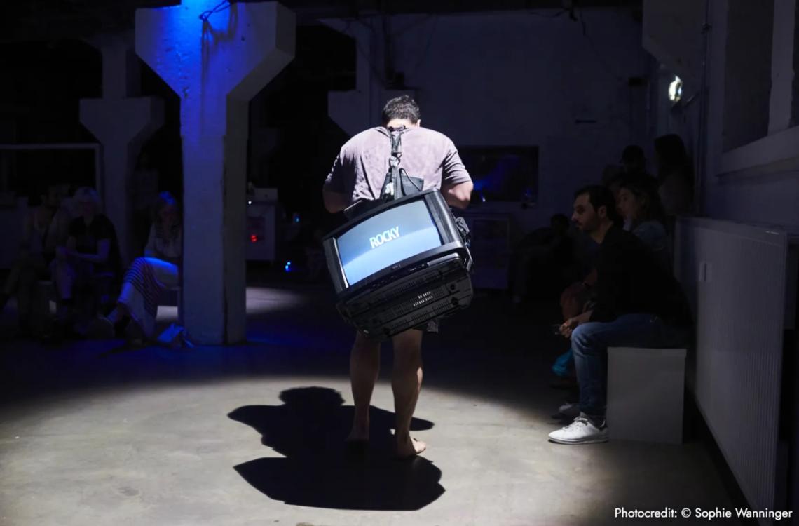 Ein Mann trägt einen laufenden Fernseher auf dem Rücken.