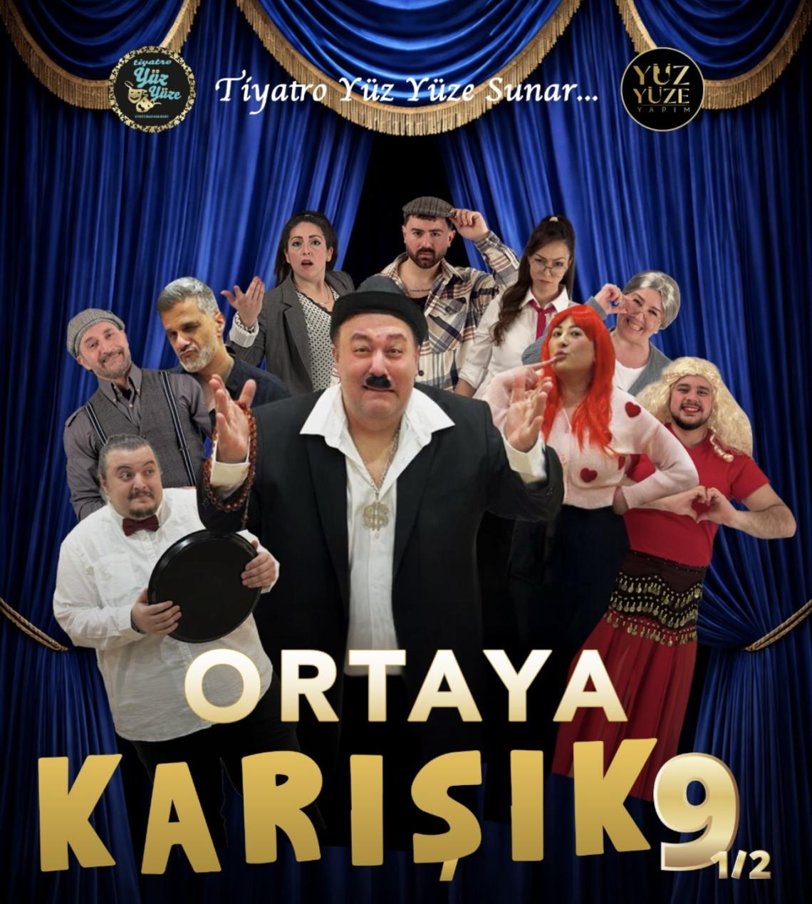 Ein Mann im schwarzen Anzug steht vor einem Theatervorhang, umgeben von vielen Figuren in diversen Kostümen.