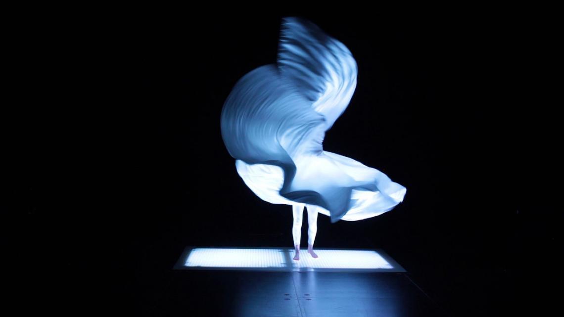 Eine Tänzerin steht mit weit schwingendem Kleid in blauem Licht.