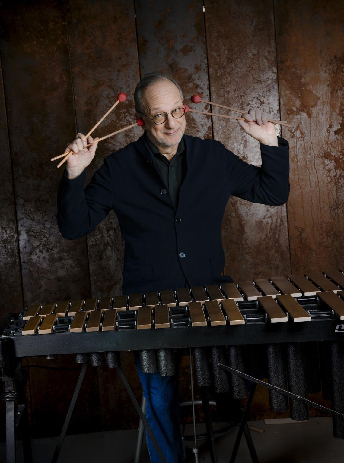 Ein Vibraphonspieler steht hinter seinem Instrument und hält sich die Schlegel in einer lustigen Geste an die Ohren.