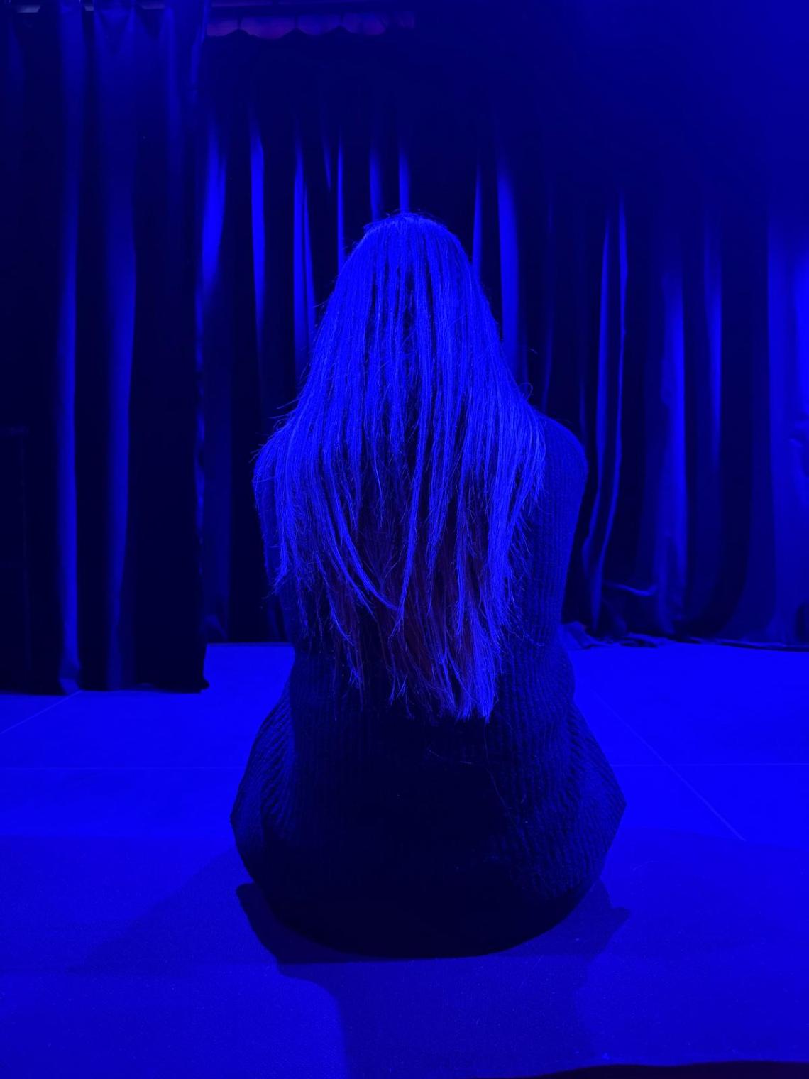 Eine junge Frau sitzt in einem Raum voll blauem Licht.