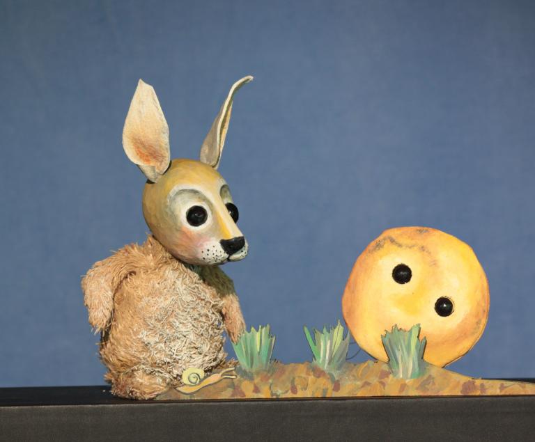 Ein Hase und ein Pfannkuchen mit Augen sitzen im Gras.