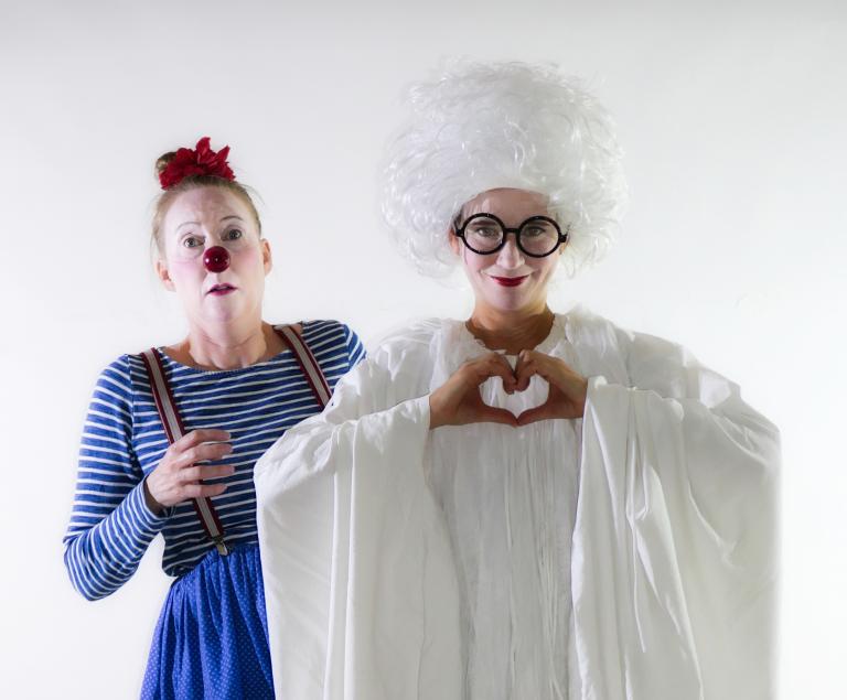 Ein weißes Gespenst zeigt das Herz-Zeichen mit den Händen, hinter ihm steht eine Clownin mit roter Nase.