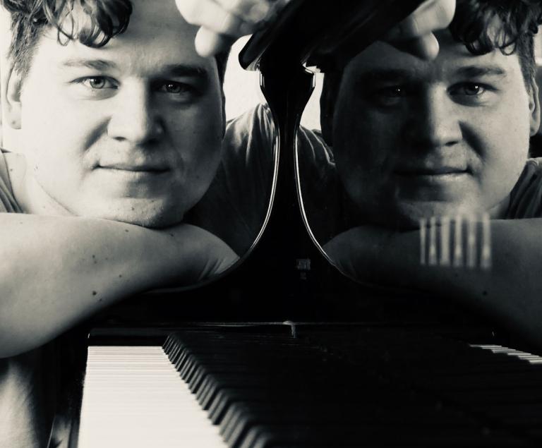 Ein Pianist spiegelt sich im Lack eines Konzertflügels.